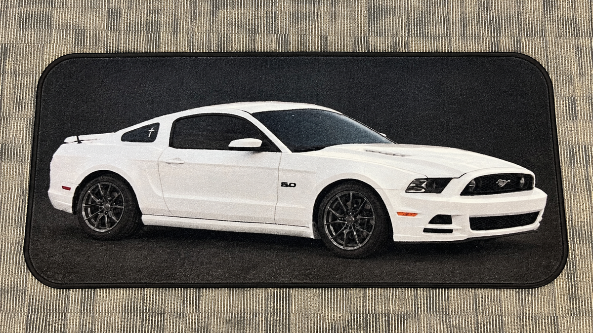 Rectangular custom rug depicting a white coupe with dark wheels on a black background, photographed on a patterned floor.